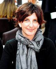 Kristy Hill smiling with medium length brown hair wearing a black long sleeve top and a gray fashion scarf with print of the Eiffel Tower 