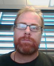 Dr. 约翰F. 桑托尔，淡红色的金色头发, 小胡子和大胡子戴着棕色的眼镜，穿着深绿色的衬衫