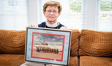 Mary Donahue sits on a couch holding a photo of her and her fellow Air Force pilots