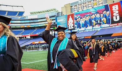 A graduate waves to the crowd while walking to her seat.