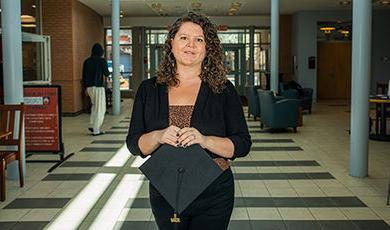 Jamie Jackson stands in the ECC lobby while holding a graduation cap.