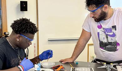 A high school student puts blackberries on a solar cell as a BSU student offers guidance.