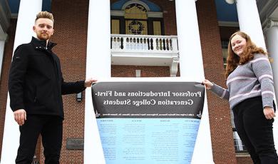 Students hold a poster of their research in front of the Boyden Hall columns